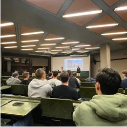Studierende sitzen in einem Hörsaal und folgen einer Präsentation an der Stirnseite.